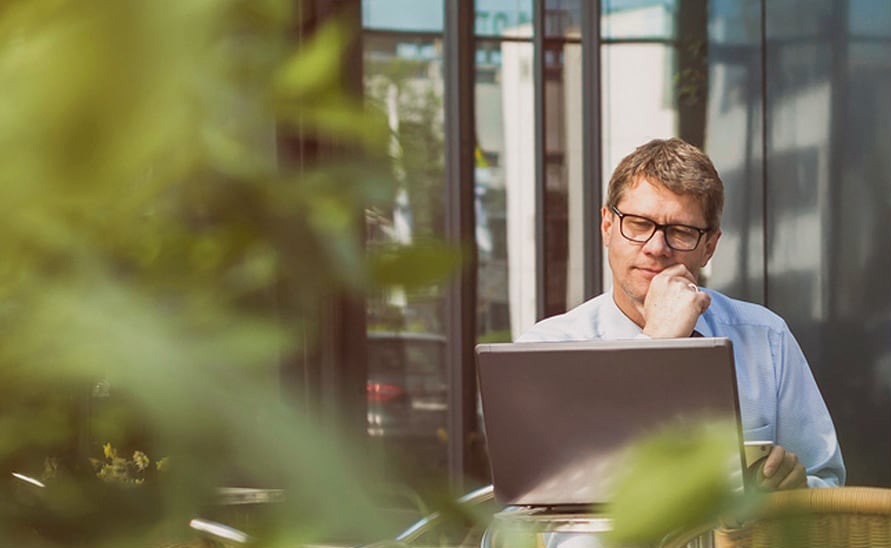 Image of man sitting at desk looking at computer with trees in the background